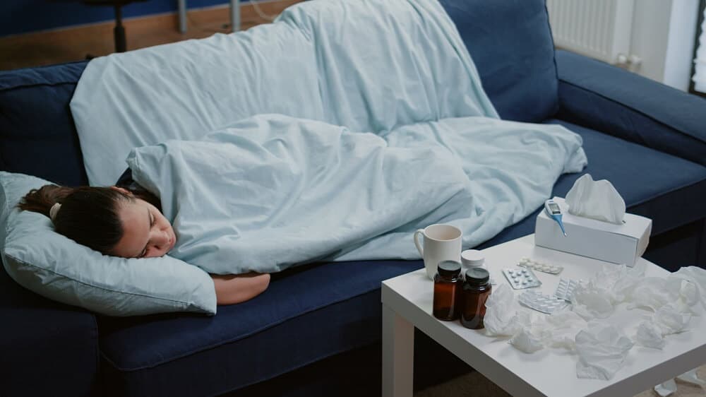 Pessoa com doença dormindo embrulhada em cobertor no sofá